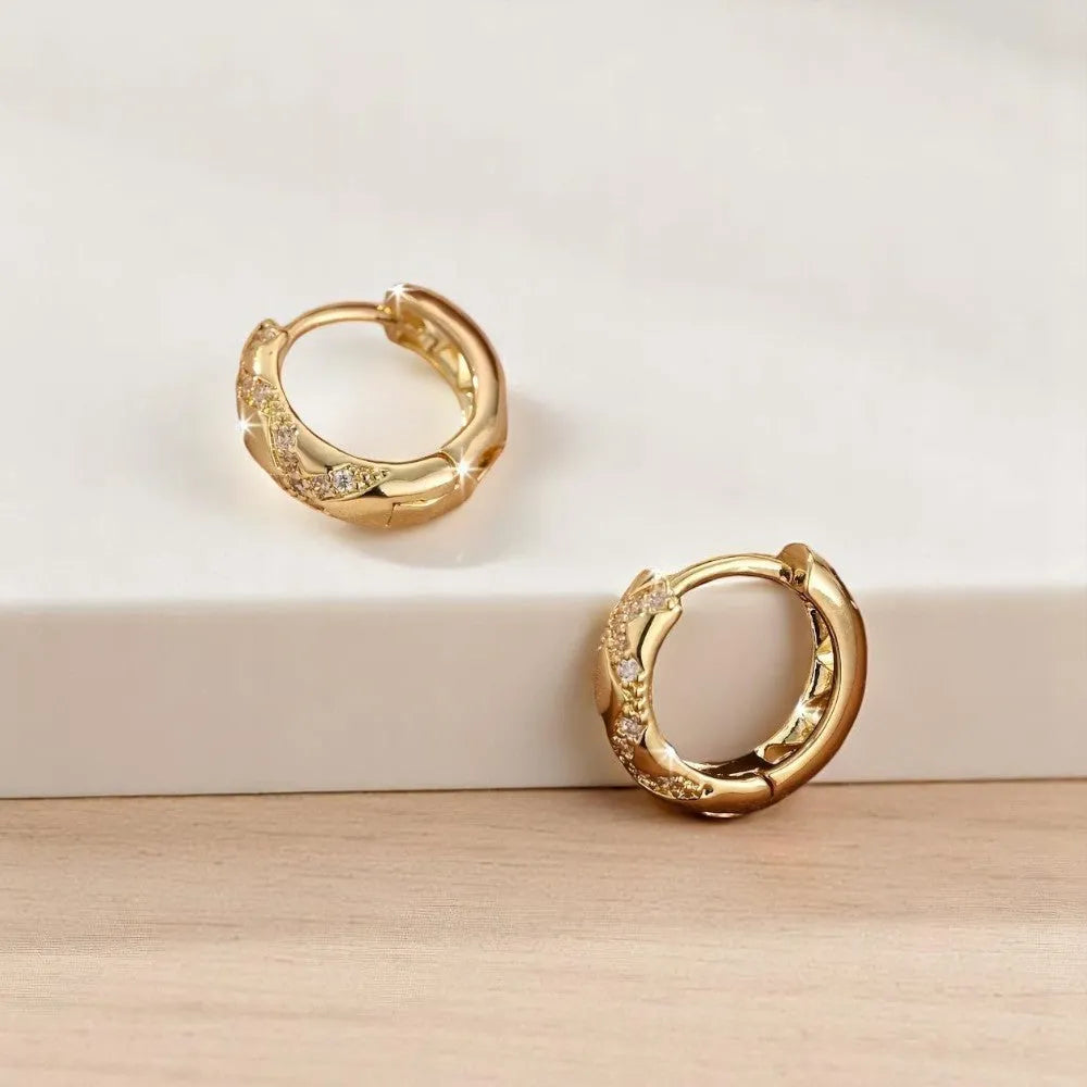 Gold hoop earrings with embedded stones on a light background